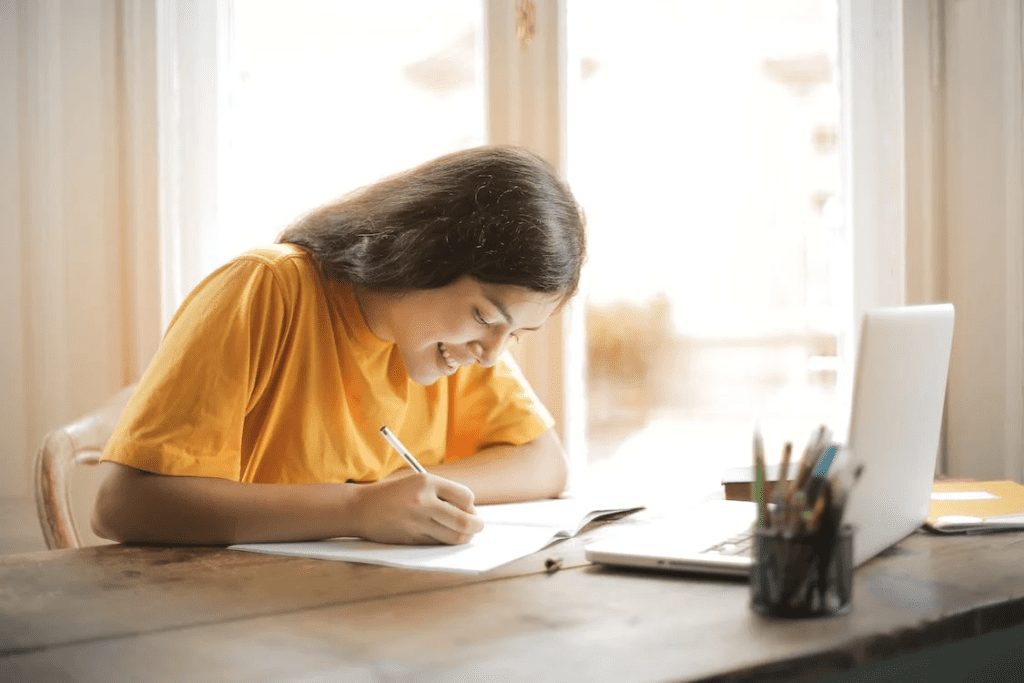 woman in a yellow shirt writing on her journal