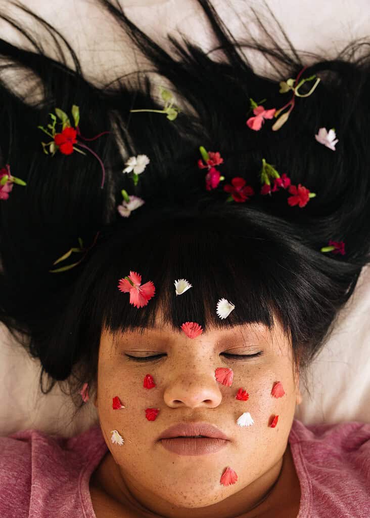 a woman laying in bed with flowers in her face and hair