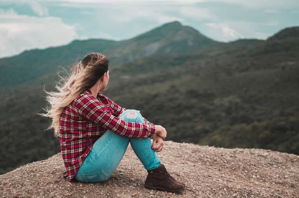 a woman sitting on a hill with a view of a mountain