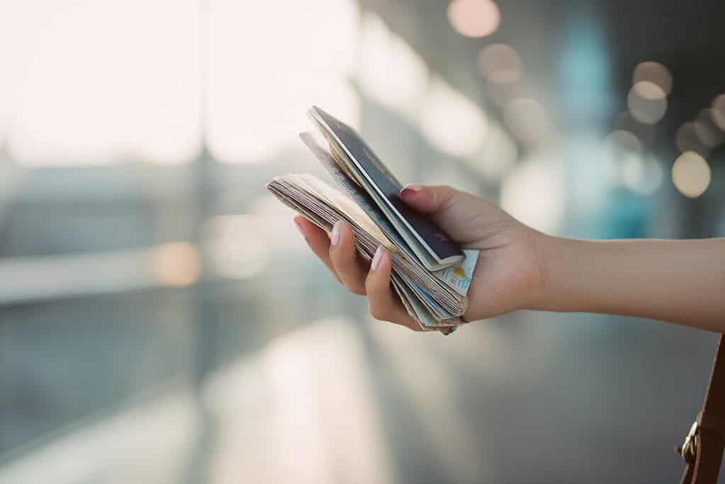 a woman’s hand holding a passport along with travel documents, folded maps, and boarding passes. 