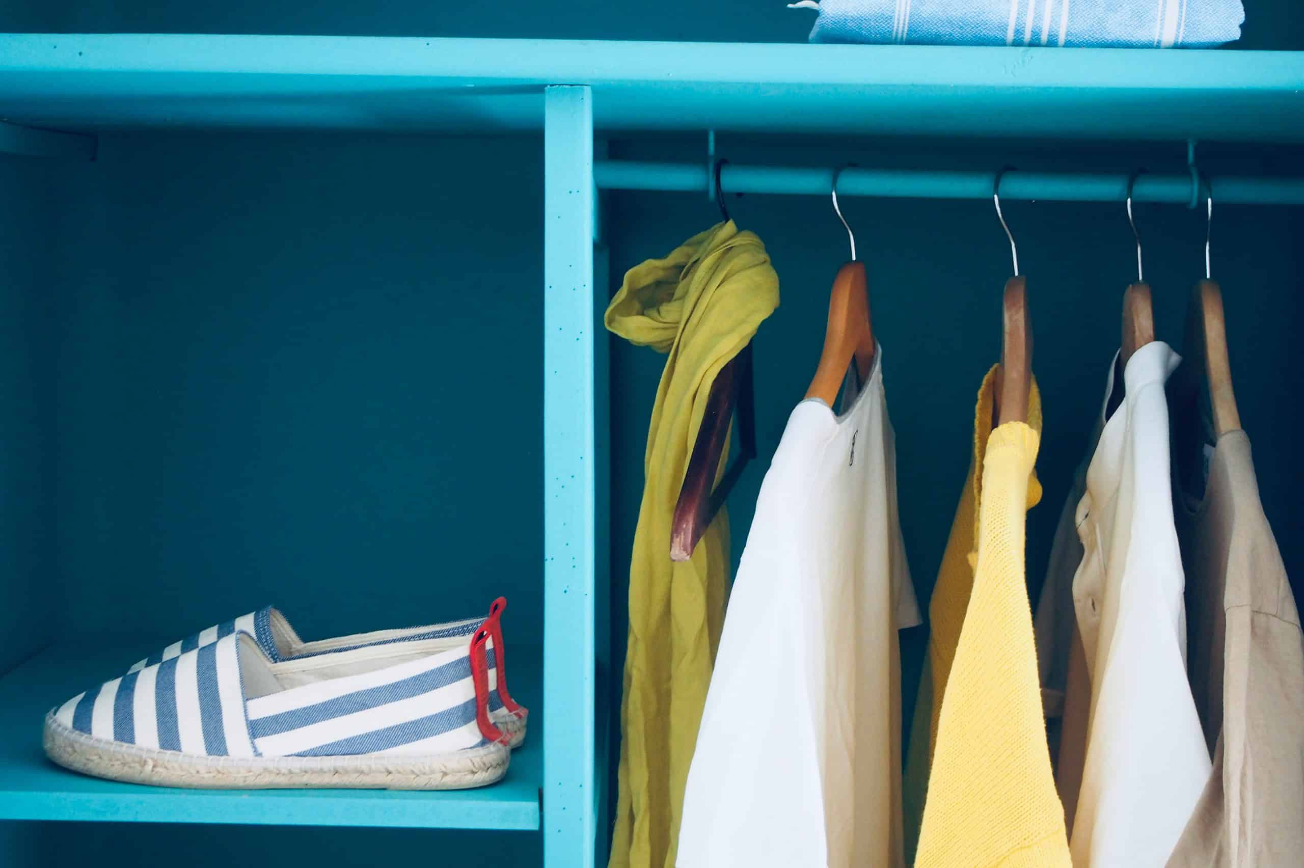 a neatly styled open wardrobe painted in a vibrant turquoise blue.