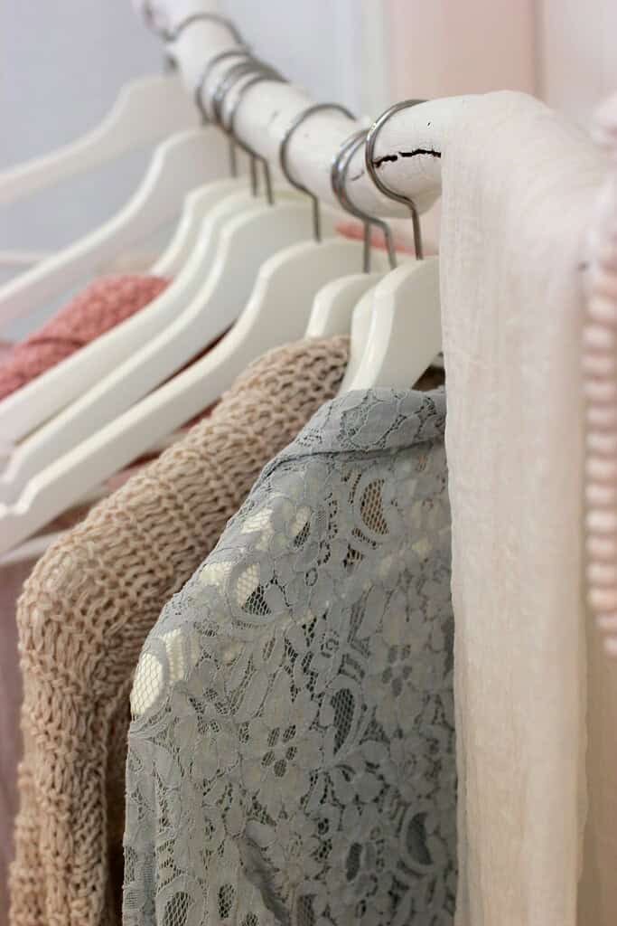 Neutral-toned clothing on white hangers featuring lace, knit, and soft fabric textures, styled on a minimalist rack for a capsule wardrobe for short women.