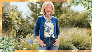 Elegant middle-aged woman in a blue cardigan and floral blouse posing outdoors in a blooming garden, showcasing chic casual fashion for women over 50.