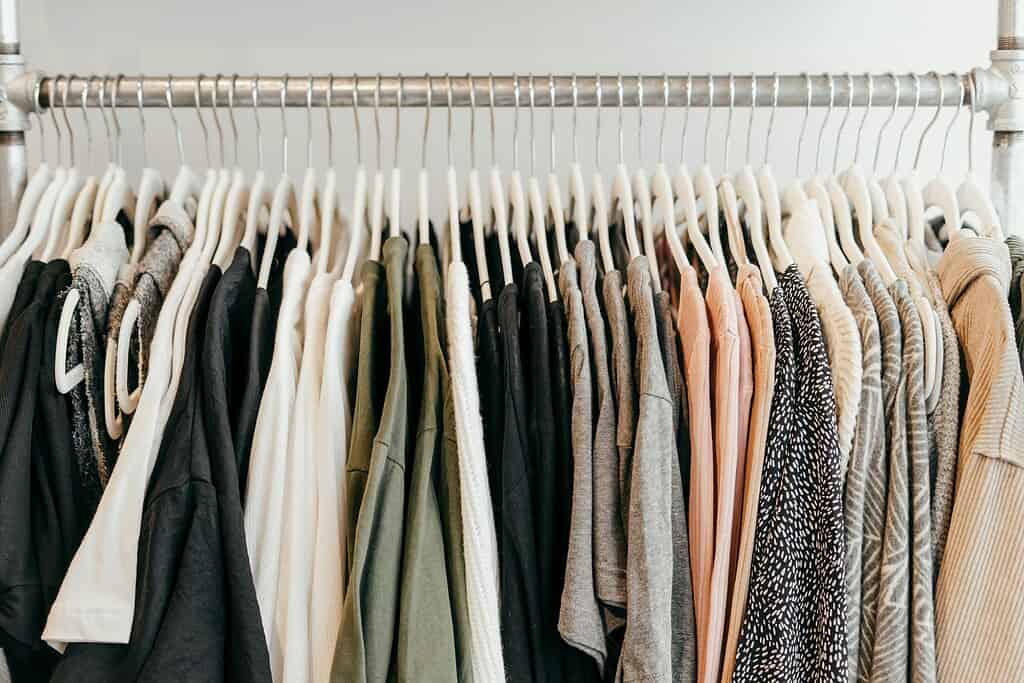 A wooden closet with neatly folded sweaters in soft neutral colors stacked on wooden shelves with soft natural light