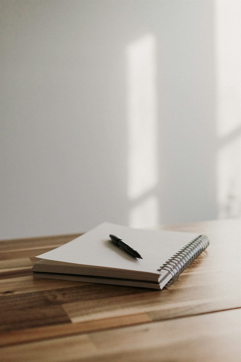 An open spiral notebook with a pen on a wooden desk