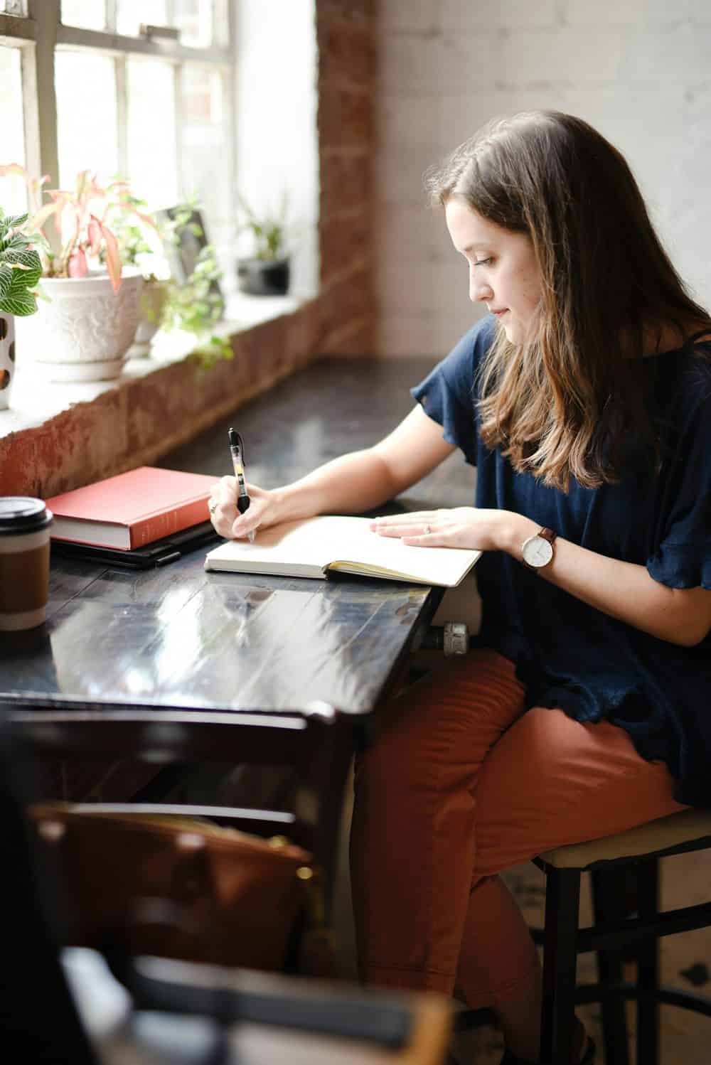 A woman writing in her journal at a wooden table by a window