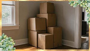 A neat stack of closed, slightly worn cardboard boxes in the corner of a room against a plain wall in soft daylight