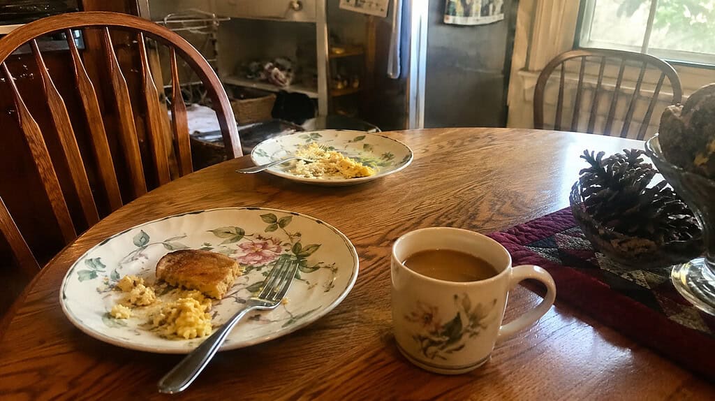 A small kitchen table set for breakfast with two floral china plates and a cup of coffee in warm morning light