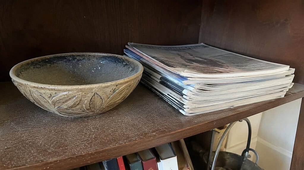 A dusty decorative bowl and a stack of old forgotten magazines on a shelf, the kind of things to let go of when decluttering