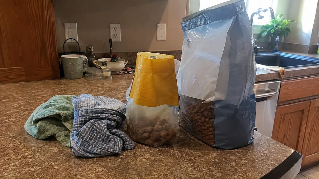 A spare bag of pet food, a half-empty treat bag, and a couple of old towels gathered on a kitchen counter in warm daylight