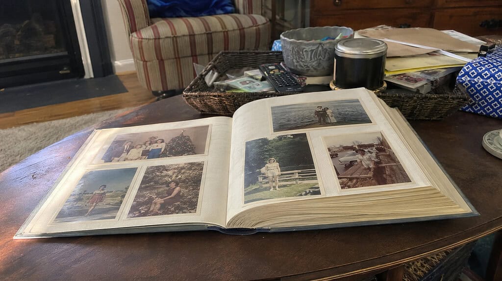 A single nicely filled family photo album lying open on a living room coffee table, showing a few treasured old family pictures on the page