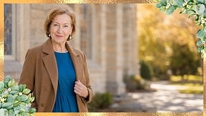 Woman in her seventies with short blonde hair wearing a teal dress and open camel coat outside a church on an autumn day, with open space for a title.