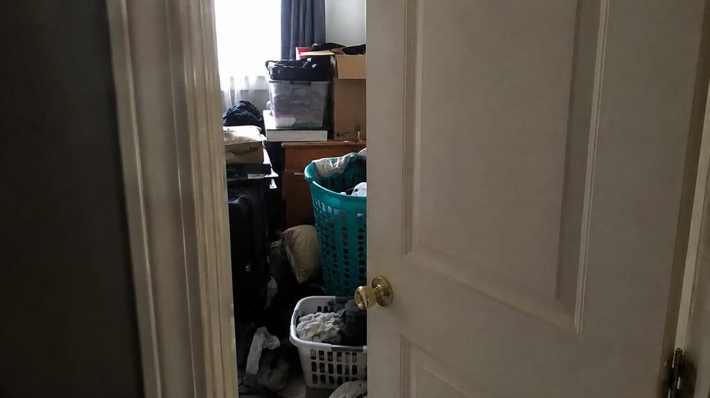 A partly closed bedroom door opened just enough to reveal a crowded, cluttered room behind it that someone would rather keep hidden