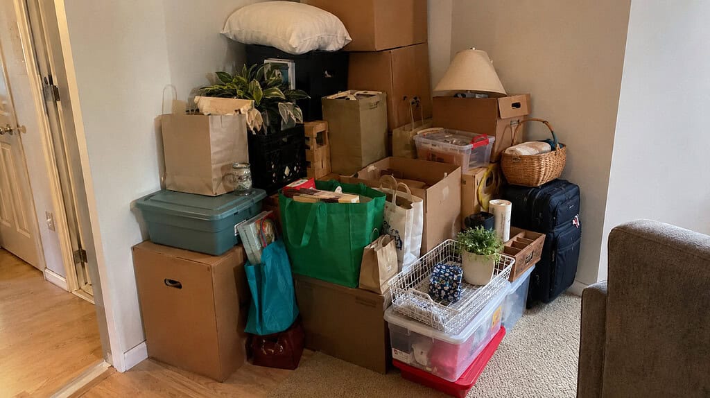 A corner of a room where boxes and bags are stacked high and spreading outward, clearly growing over time with no room left