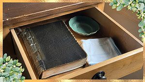 A worn old family Bible with a taped spine sitting closed in an open nightstand drawer in warm morning light