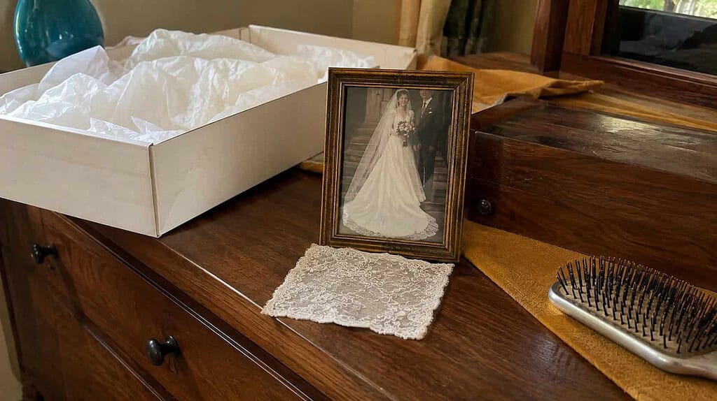 A small framed wedding photo and a kept square of ivory lace on a dresser beside an empty old wedding dress box