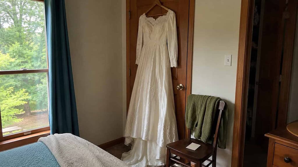 An ivory old wedding dress hanging on a bedroom door above a chair with a small folded note, offered to pass down