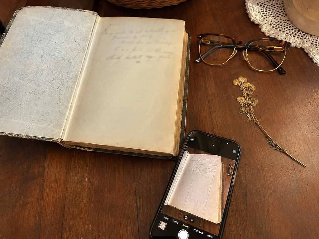 A smartphone beside an old family Bible open to its front cover, set up to photograph the record page