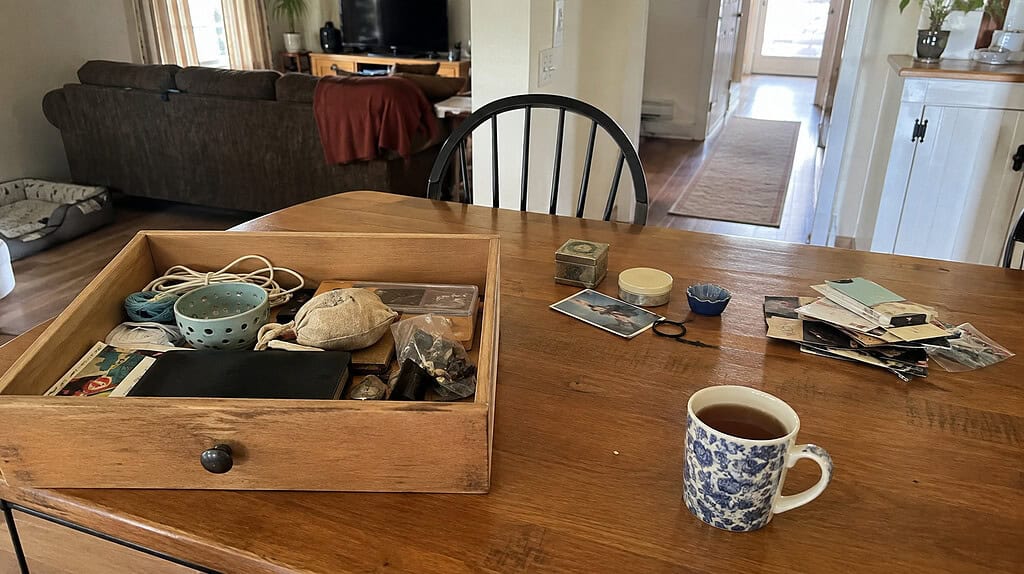 One open drawer being gently sorted on a table, with a small keep pile and a small let-go pile and a warm mug of tea beside it