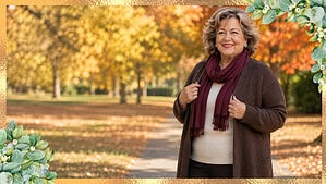 A smiling plus-size woman in her 60s outdoors in a chocolate cardigan, cream knit, and burgundy scarf on a warm autumn day.