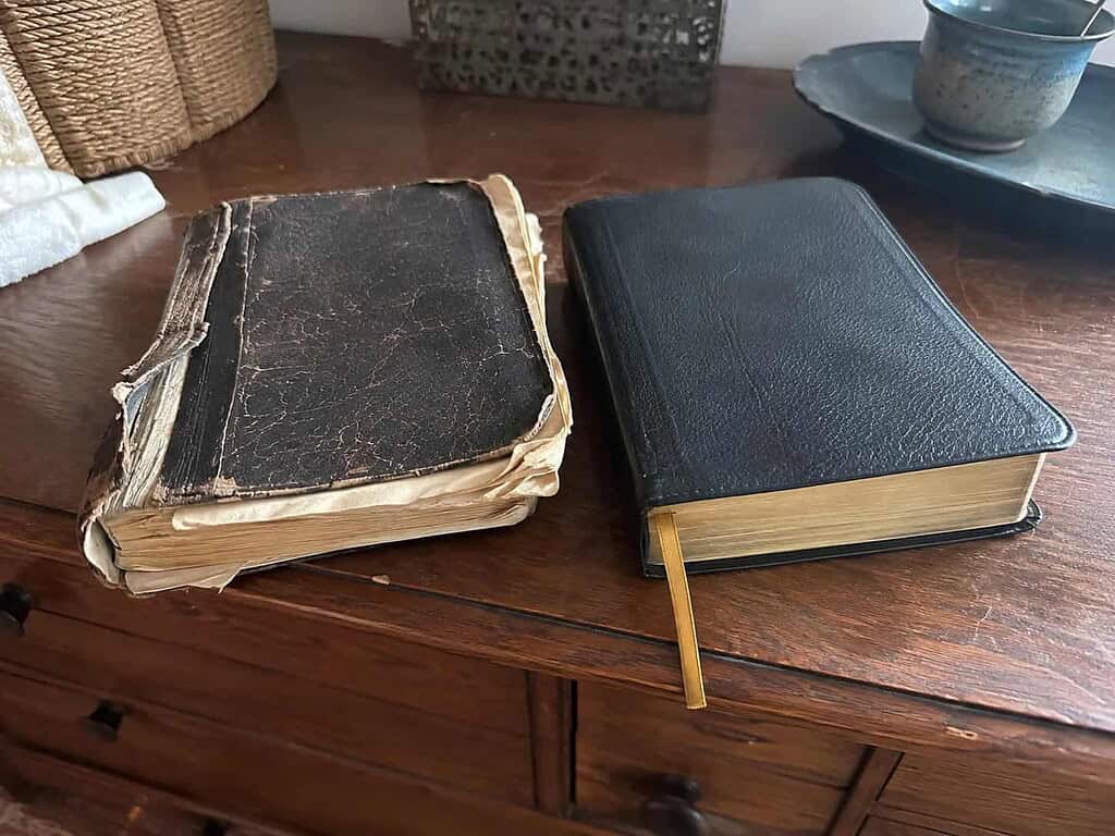 Two old Bibles on a wooden dresser, one with a broken spine and loose pages and one still intact with a ribbon bookmark