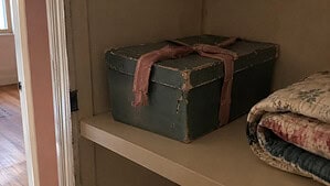 A worn old shoebox of letters tied with a faded ribbon, sitting closed on a quiet closet shelf