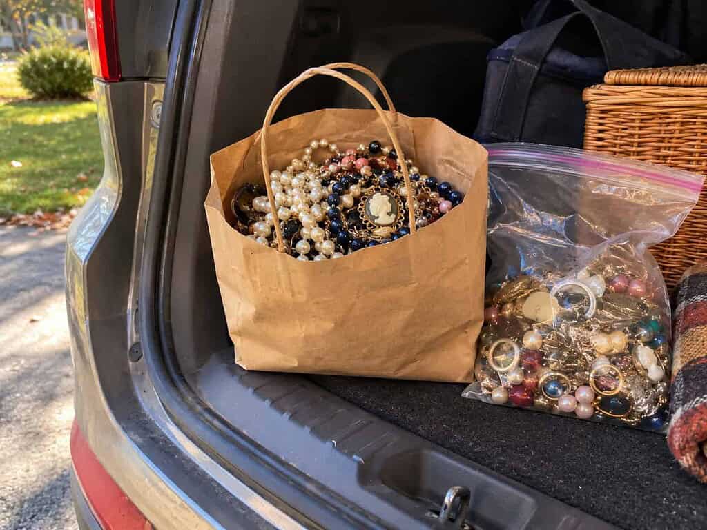 A paper bag of costume jewelry and a clear bag of broken pieces in an open car trunk, ready to drop off.