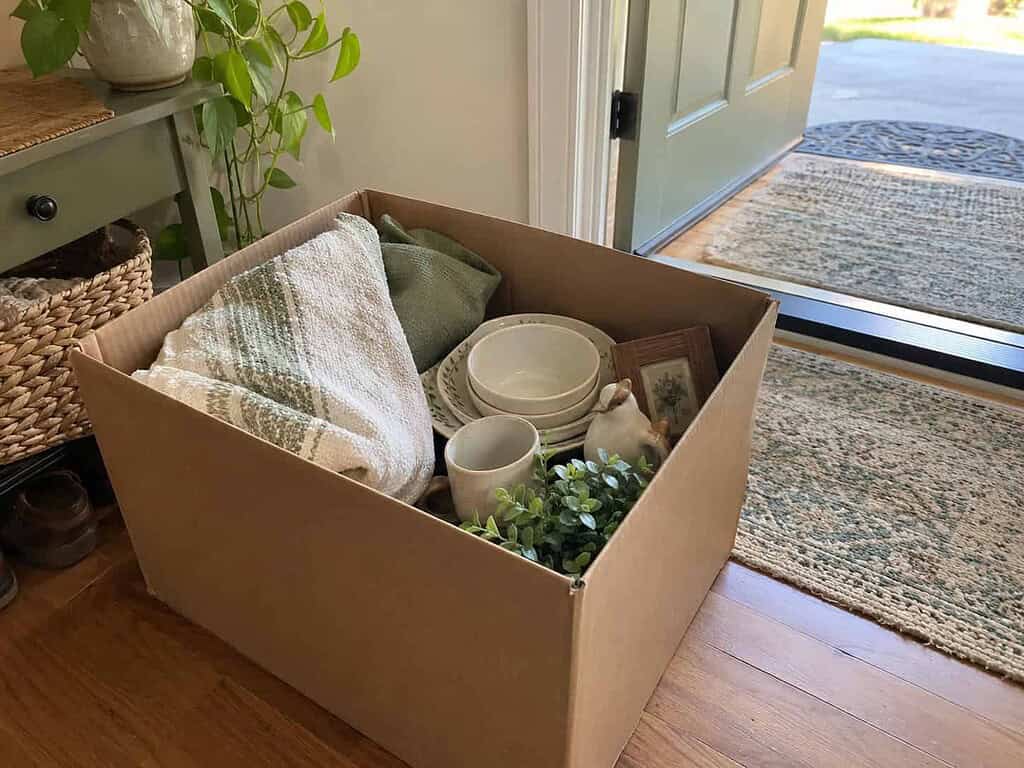 A cardboard donation box of linens, dishes, and knick-knacks sitting by the front door, ready to give away