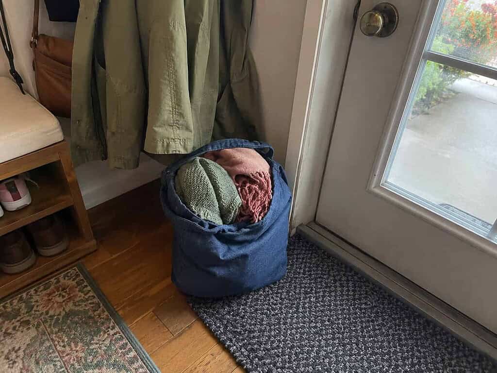 One modestly filled donation bag set by the front door, ending by taking a bag out of the house