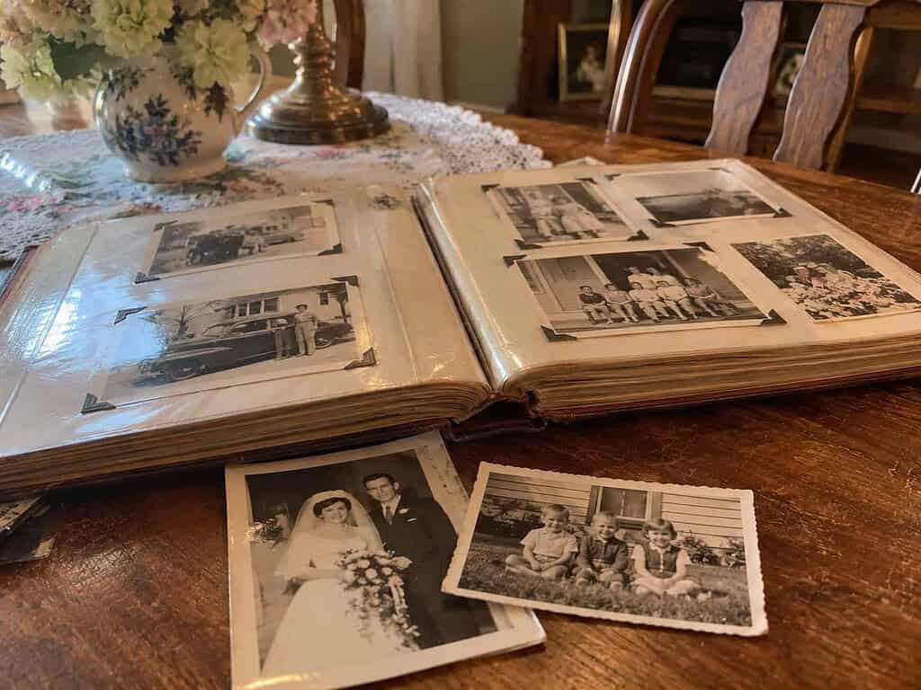 An open family photo album and loose old photographs on a table, where family history really lives