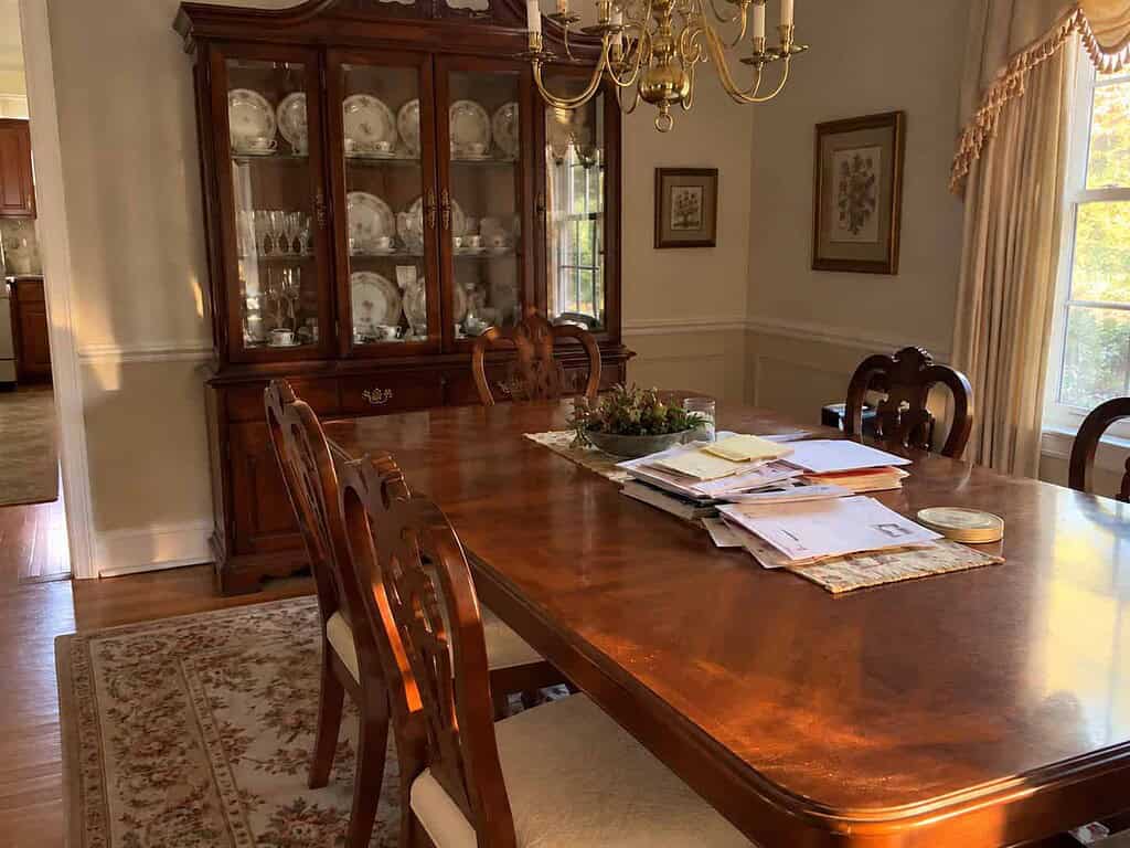 A formal dining room table piled with mail in front of a china cabinet full of matching dishes
