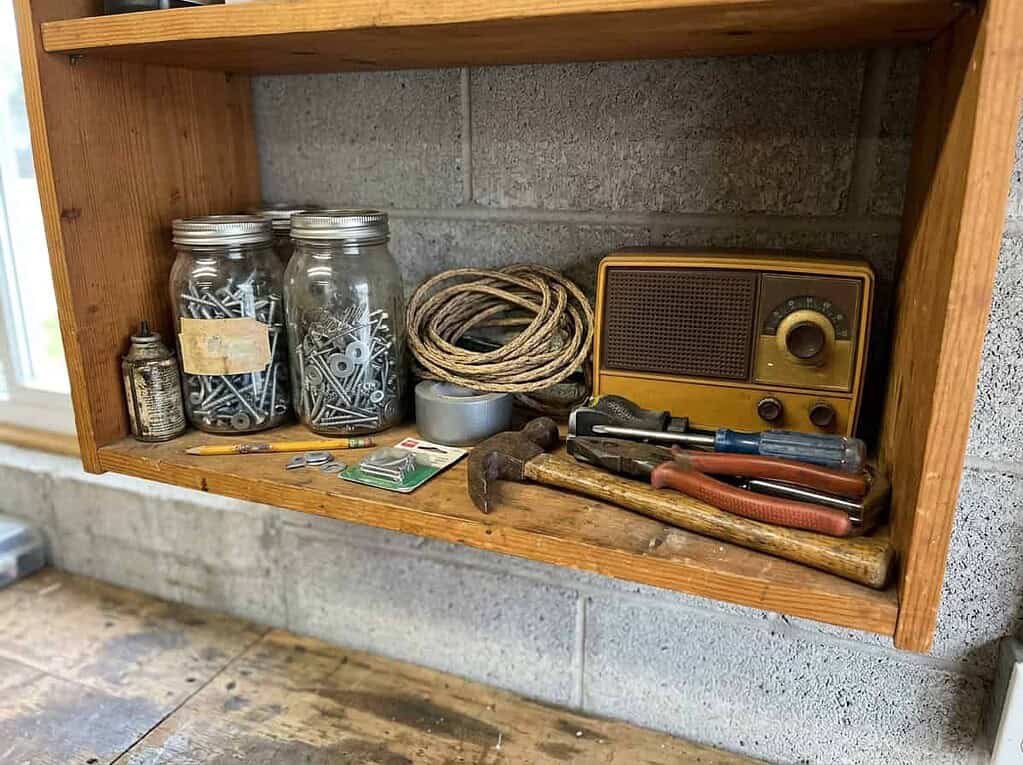 A lived-in garage shelf of a husband's kept jars, cords, and tools, forty years of "we might need it"