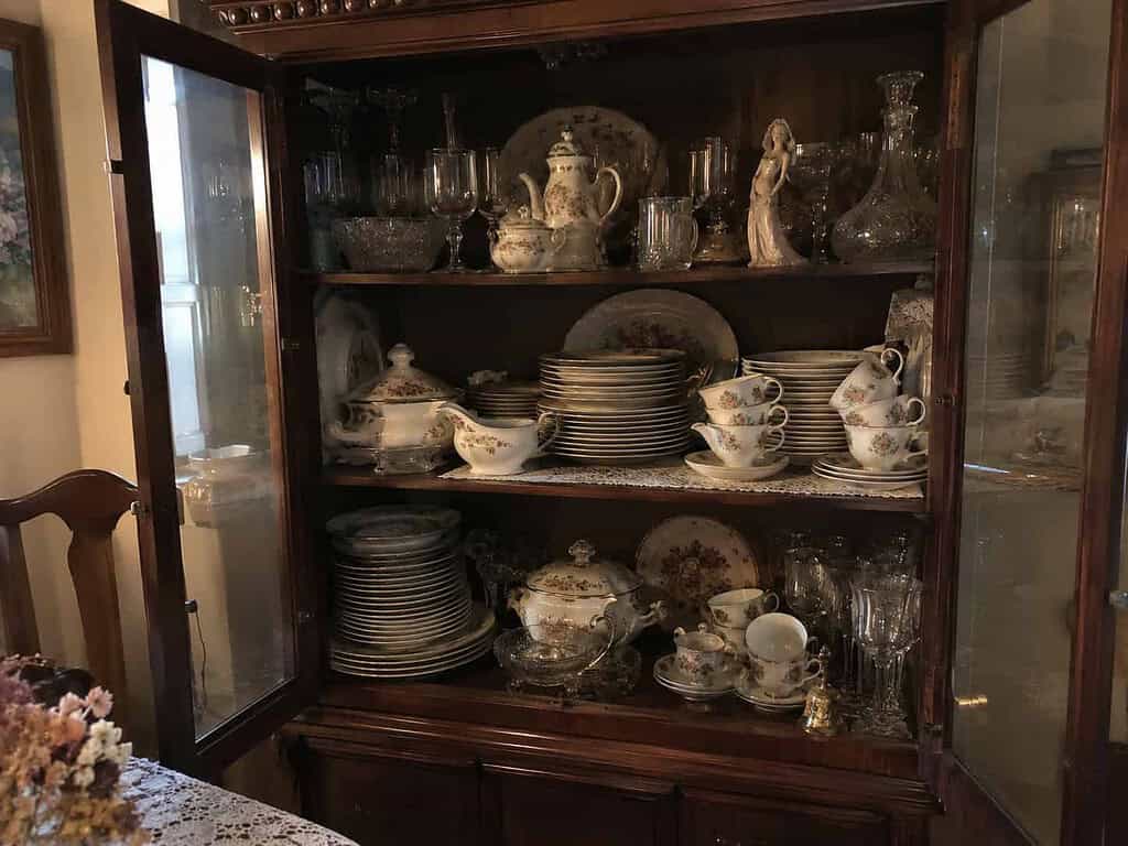 A china cabinet packed full of formal dishes and a dusty figurine, kept but rarely used