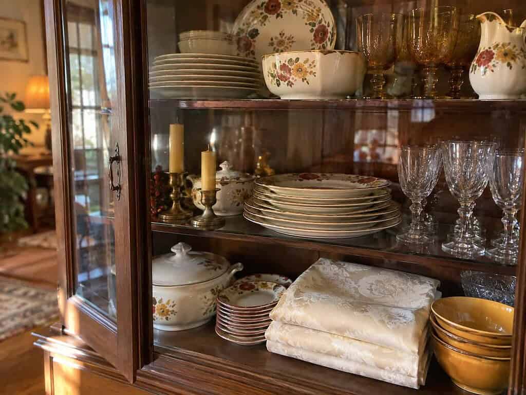 A china cabinet holding good dishes, a folded fancy tablecloth, and unburned candles all saved for a special occasion