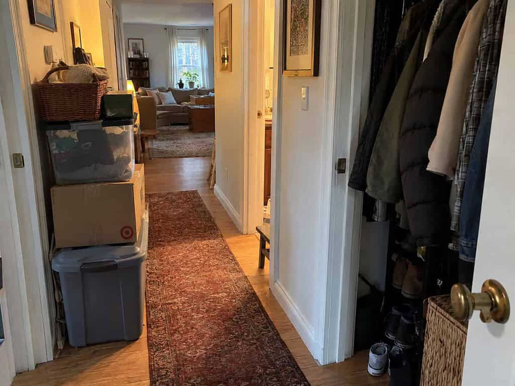 A lived-in hallway with stacked boxes and a full coat closet in an ordinary home, holding more than the household still needs