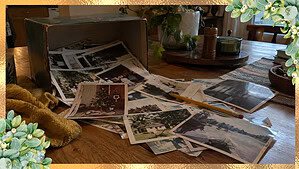 An open shoebox spilling loose faded family photos onto a wooden table with a pencil resting on top, ready for labeling old family photos