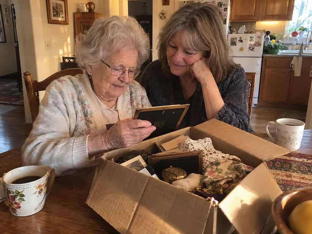 A woman in her 80s and her daughter sorting one box of keepsakes together at the kitchen table over coffee