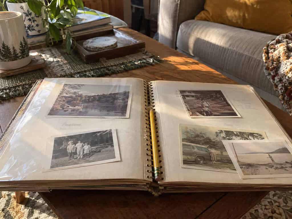 An open family photo album on a coffee table with a few labeled old prints on the page and a pencil resting in the fold