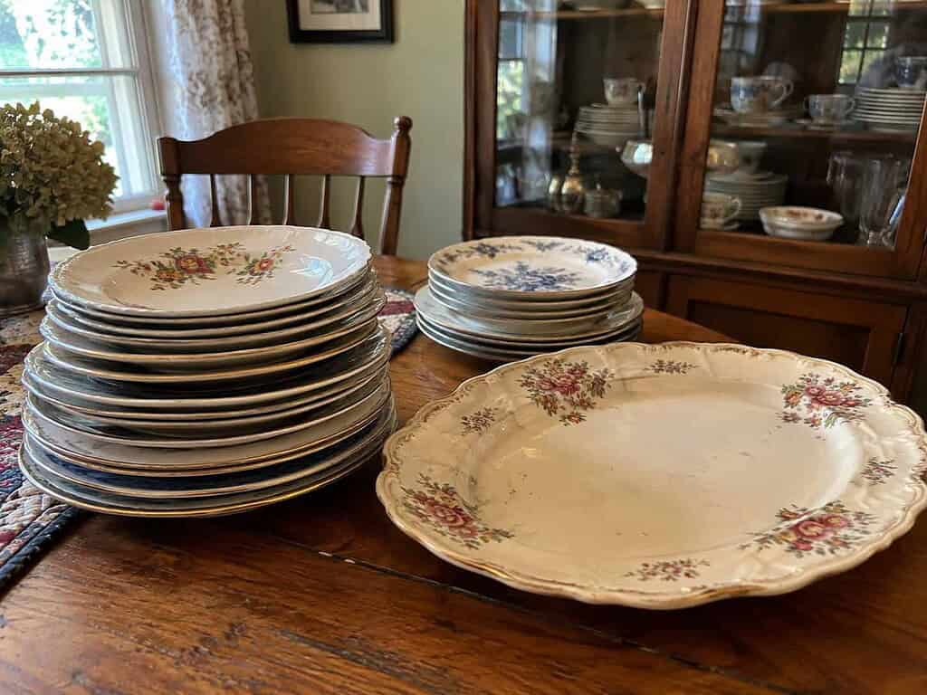 A stack of old mismatched inherited plates and a serving platter on a wooden dining table