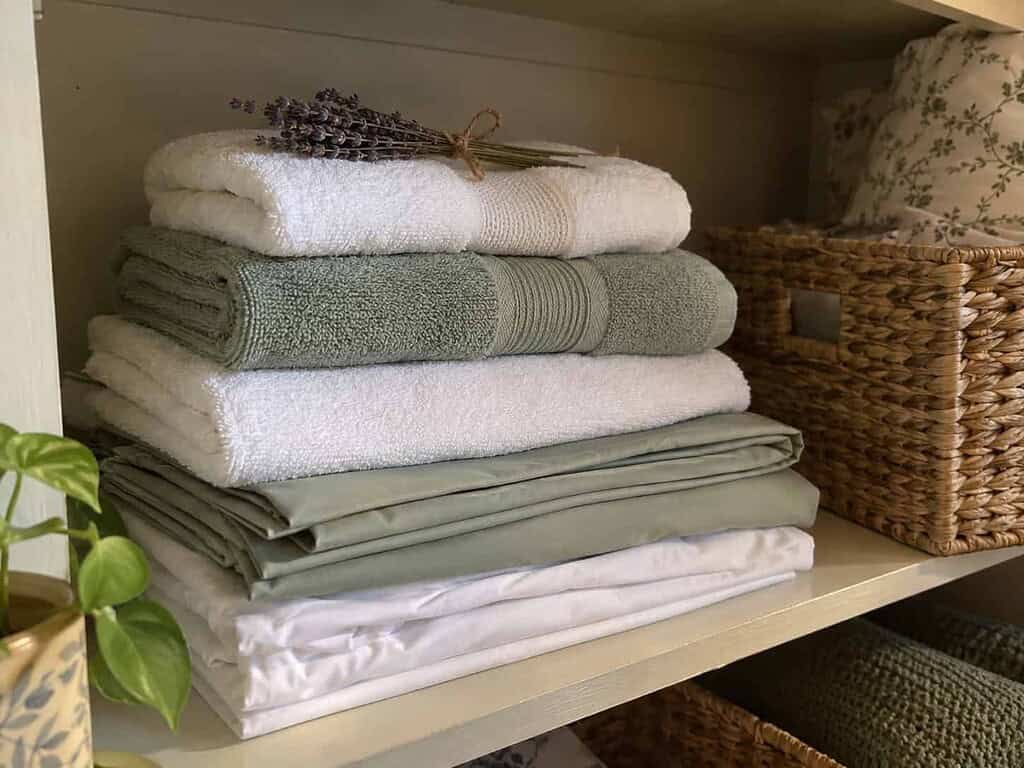 One neat folded set of guest towels and sheets on a shelf with a sprig of dried lavender on top