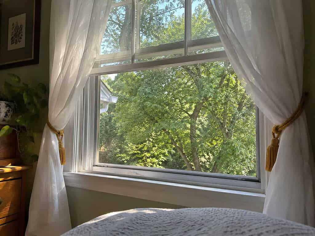 An open window with sheer curtains lifting in the breeze and bright morning light coming in