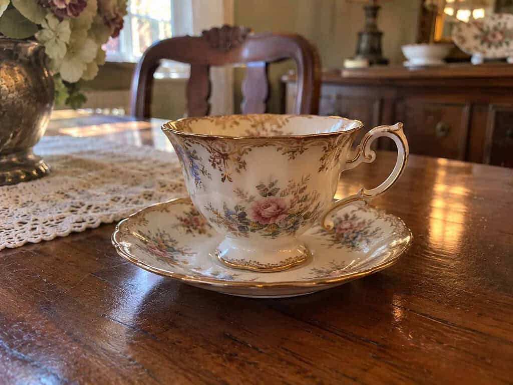 A single ornate old china teacup and saucer on a wooden table, pretty but dated