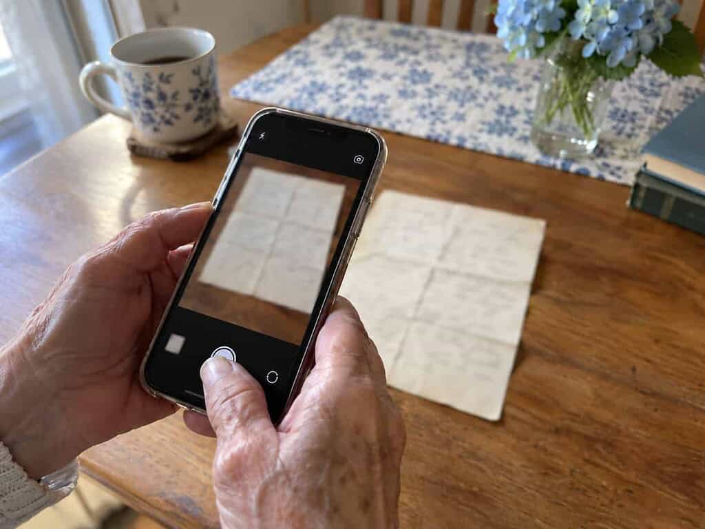 An older woman's hands photographing an old handwritten letter with a phone to make a digital copy