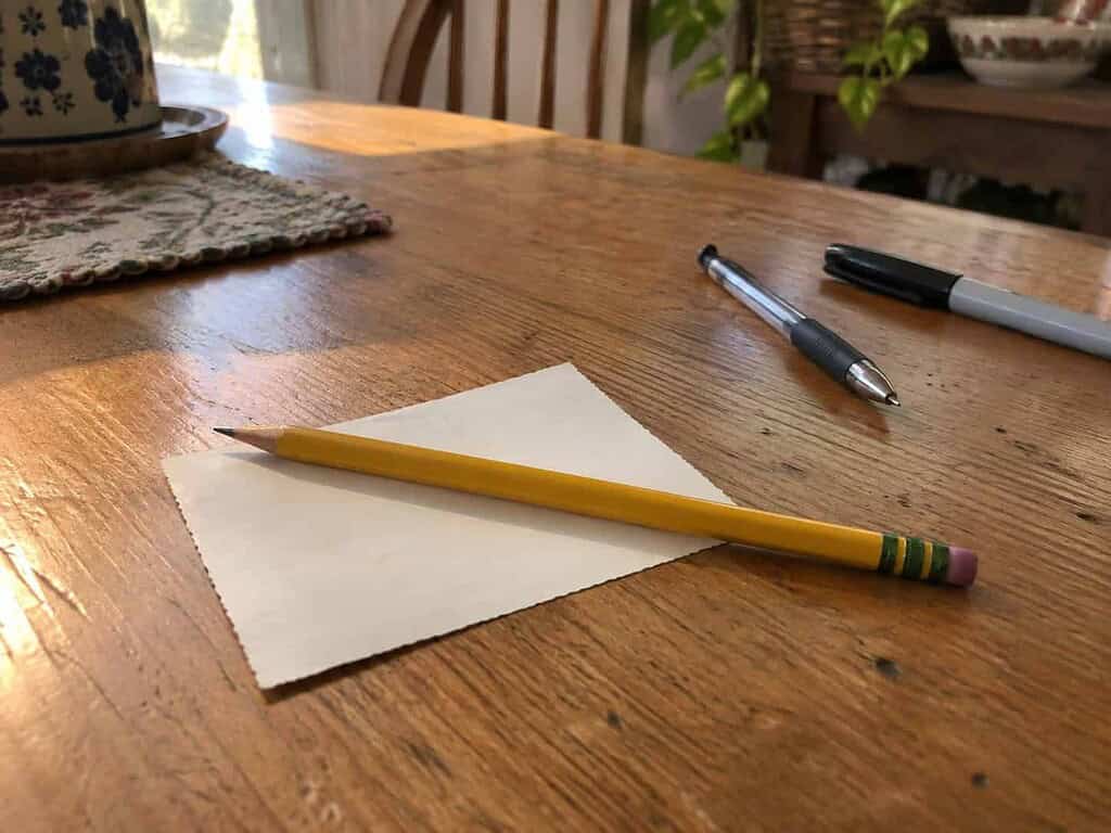 A soft yellow pencil resting on the back of an old photo with a ballpoint pen and marker set aside, showing the safe tool for labeling photos