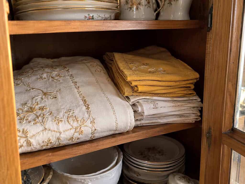 A folded fancy tablecloth and cloth napkins tucked in a cabinet, saved for special occasions