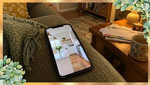 A phone on a couch showing a perfect magazine kitchen while the real lived-in living room around it holds a throw and a stack of mail