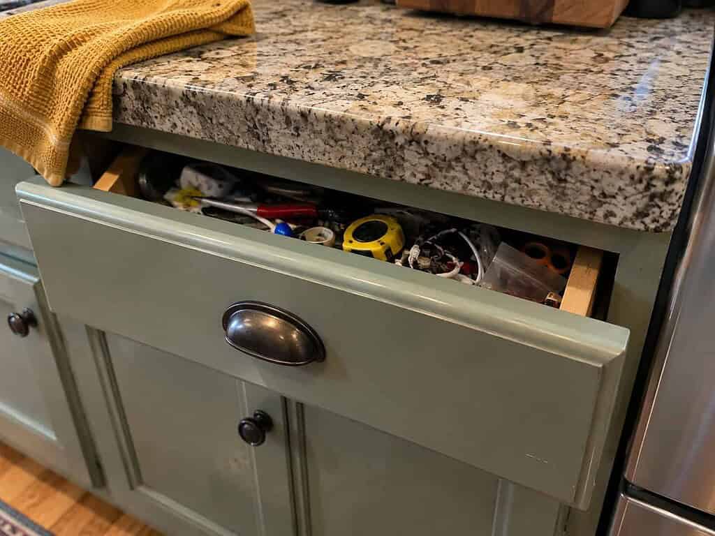 A kitchen junk drawer opened just a few inches, stuck on the jumble of small items inside