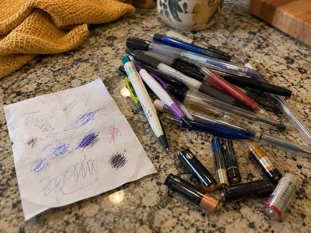 A scrap of paper with test scribbles beside a heap of dried-out pens and dead batteries to be tossed