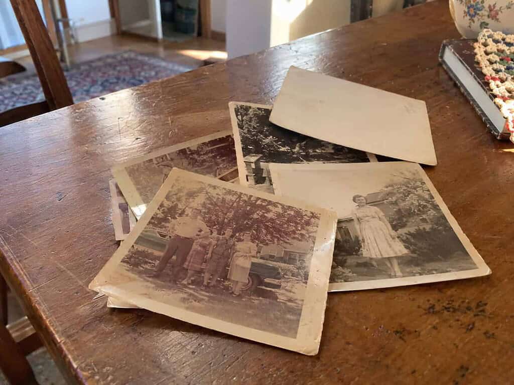 A small separate pile of very old faded photos set aside on a table, one turned over with a faint unreadable pencil mark near the edge