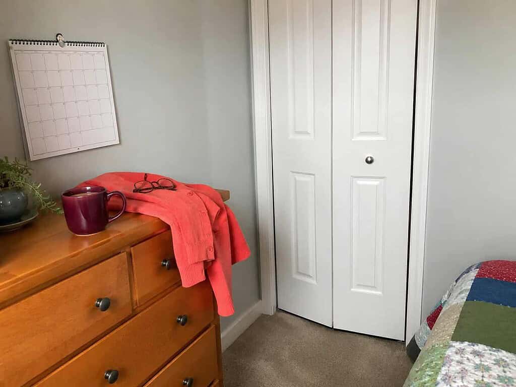 A closed closet door with a coffee mug on a nearby dresser, the perfect time to declutter that never comes
